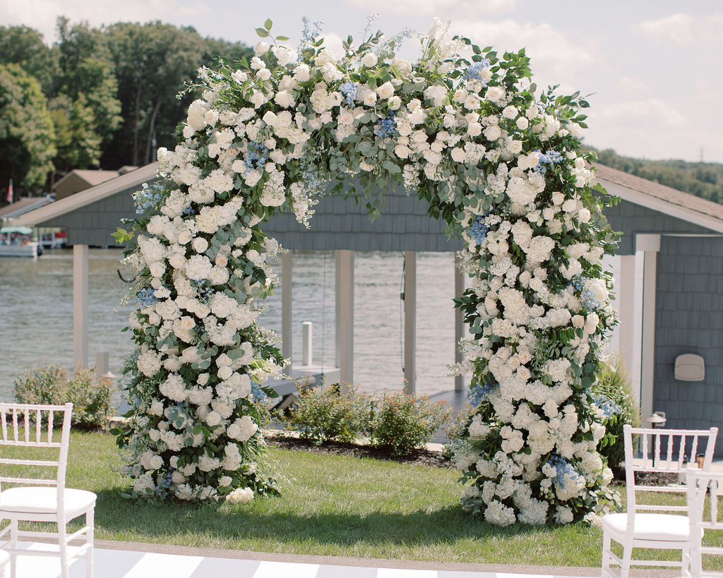 Blue and White Floral Arch in front of Ohio boat house at a lake wedding